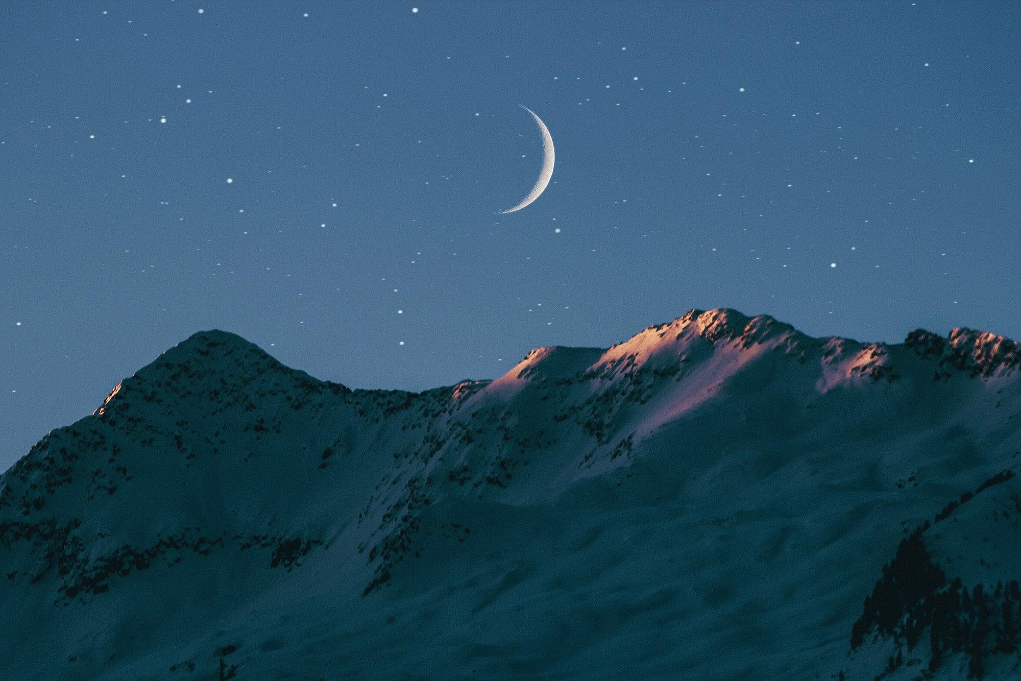 Crescent moon illuminating snow-capped mountains under a starry sky, evoking a sense of nighttime serenity