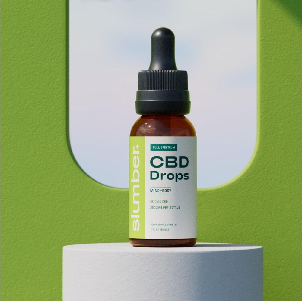 An amber bottle labeled 'Slumber Full Spectrum CBD Drops' for mind and body, with 66.7 mg CBD and 2000 mg per bottle, placed on a white surface against a green background.