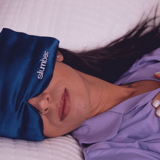 Person wearing a blue satin headband with 'slumber' logo, lying in bed.